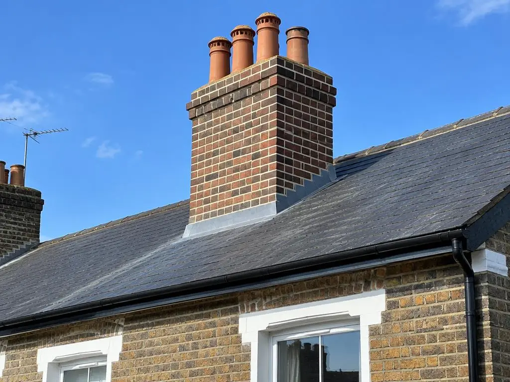 Chimney Pointing & Repairs in Yorkshire Freshly repointed brick chimney stack with terracotta pots on a slate roof