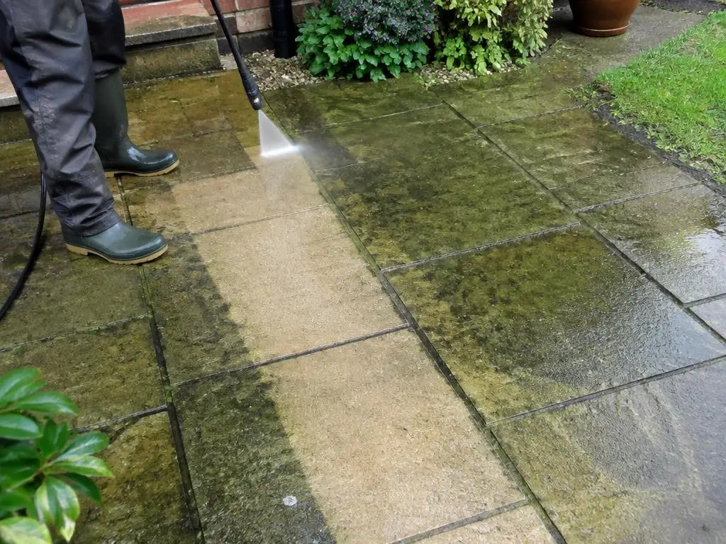 Patio Cleaning in Yorkshire Patio being pressure washed, showing a clean stripe through algae-covered paving slabs